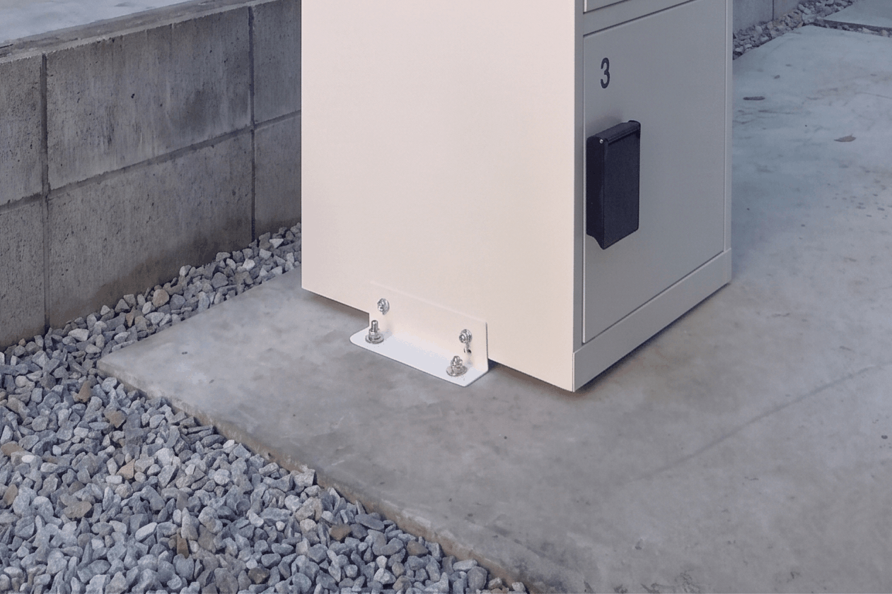 コンクリート上に設置された宅配ボックスの足元部分で、金具とボルトにより地面へ固定された設置状態